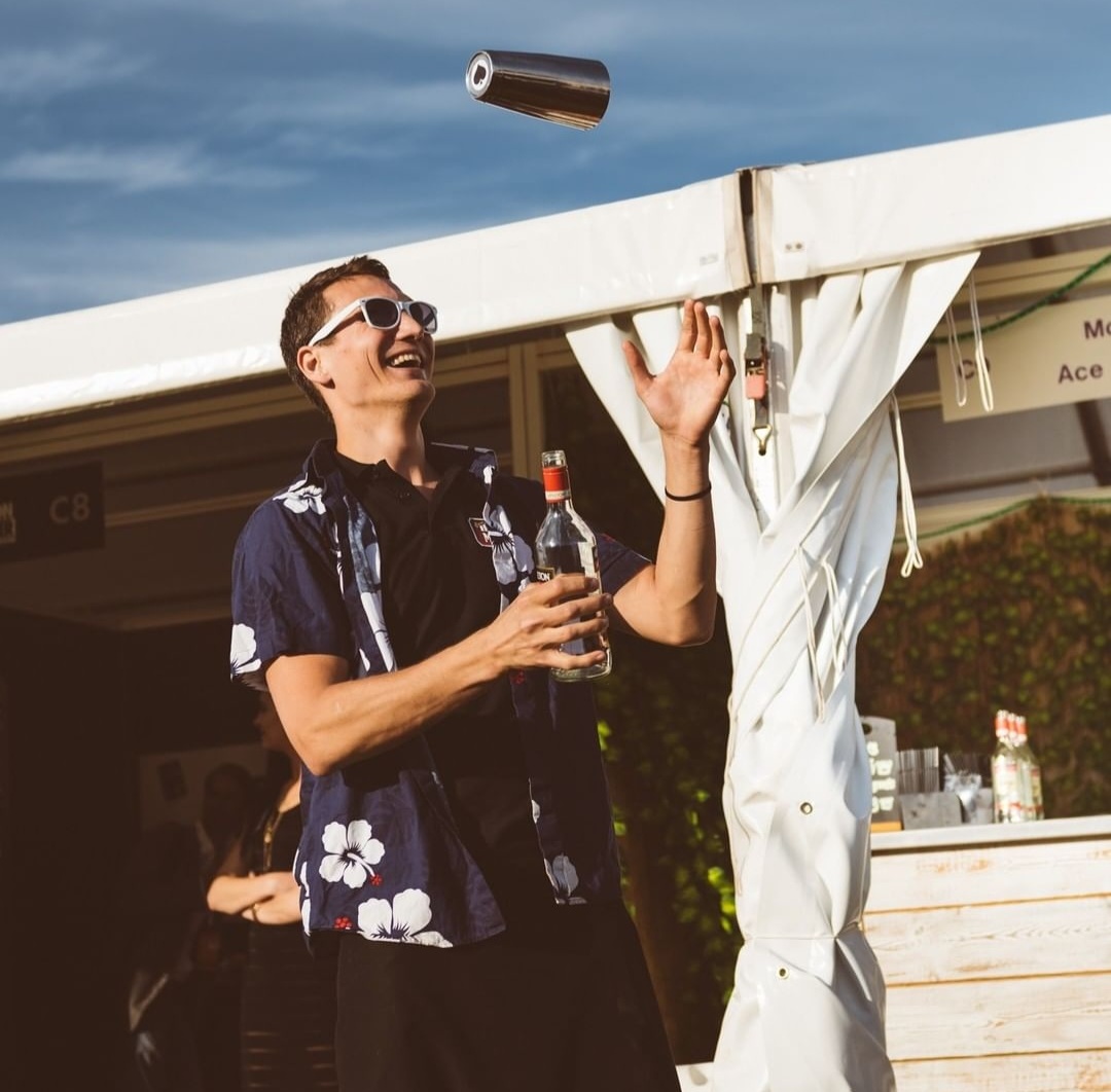 A flairbartender in a Hawaiian shirt throwing a cocktail shaker in the air
