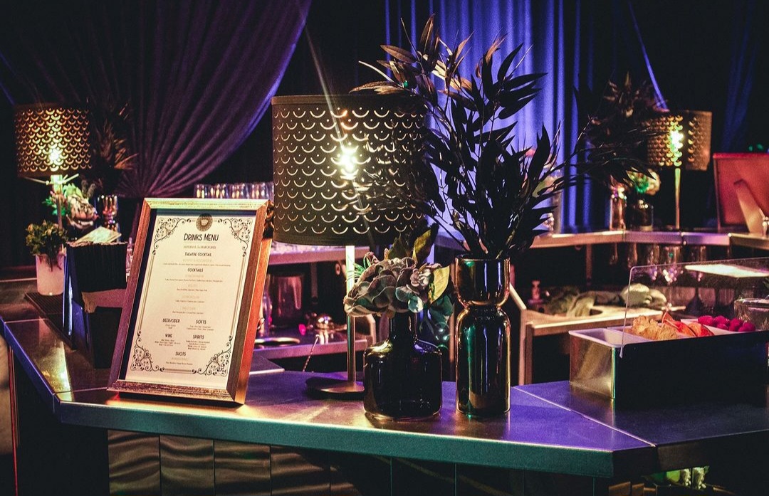 Drinks menu and floral arrangements in black vases on top of a bar.