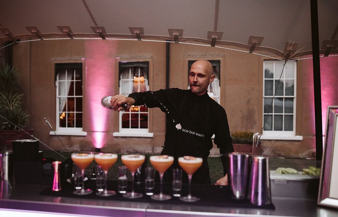 A flair bartender behind a bar pouring a row of Espresso Martinis.