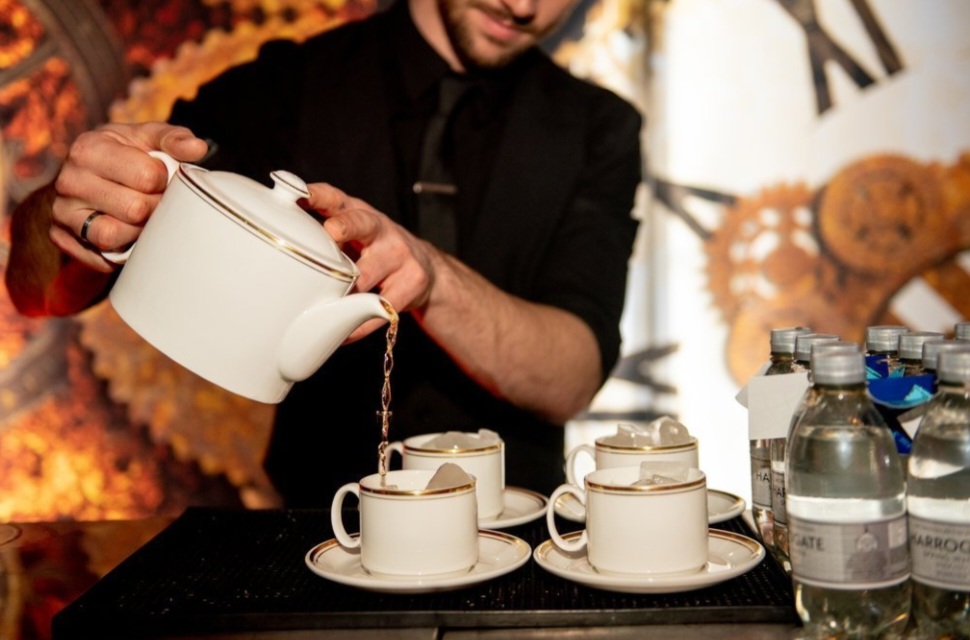 A Mad Hatter bar tender for Alice in Wonderland themed events, pouring cocktails from a teapot in to teacups.
