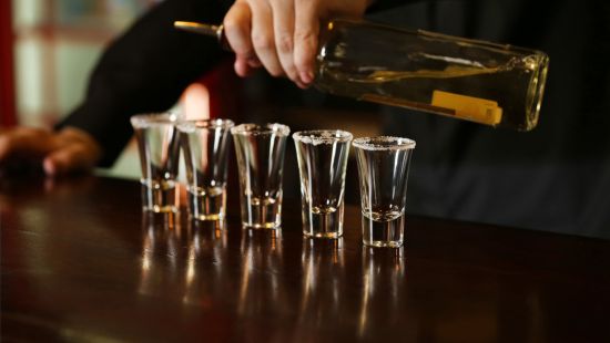 A male barender's hand pouring a round of shots at a bar.